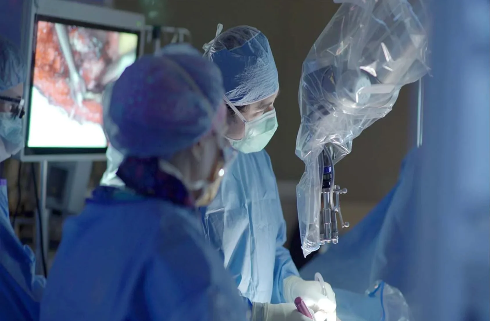 A spine operation in progress, the surgical field on the monitor behind the surgeons